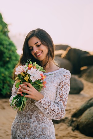 bride with bouquet in hands is standing on beach and smilingの写真素材