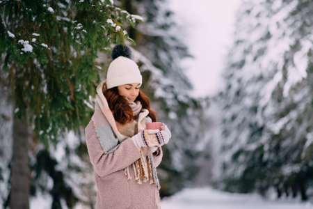 joyful female stands in snowy park with cup of coffee in hands