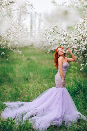 Happy young red-haired woman enjoying spring in blossoming gardenの写真素材