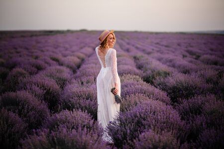 Young woman in white dress walks through blooming lavender field at sunsetの写真素材