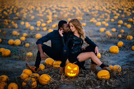 Couple sitting in field near scary face pumpkin, concept halloweenの写真素材