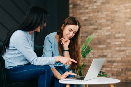 Young woman points her friend at laptop screenの写真素材