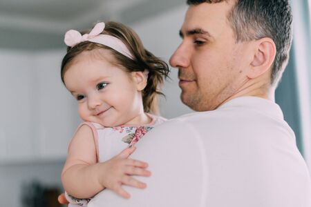 Little smiling girl in arms of her young father at homeの写真素材