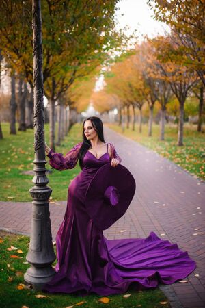 young woman in vintage silk dress is standing in autumn parkの写真素材