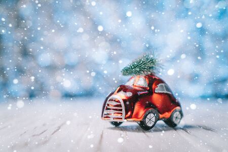 Little red toy car carries a Christmas tree on a blue blurred backgroundの写真素材