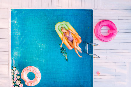 Young female basking in sun while swimming in pool on an air mattress, drone shot