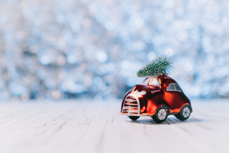 Little red toy car carries a Christmas tree on a blue blurred background