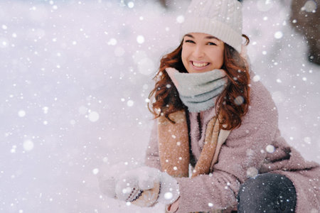 Happy young woman sculpts a snow ball while playing in a park on a winter day.