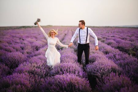Happy laughing newlyweds are walking on a blooming lavender field at sunset, general planの写真素材