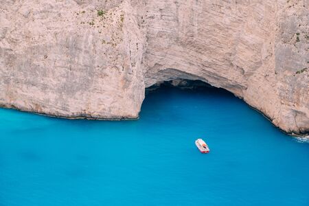 A small boat floats on water near steep high cliffs.の写真素材