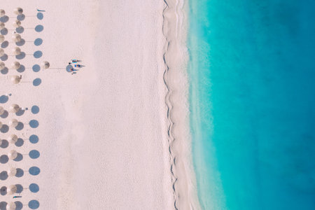 Top-down aerial view of a clean beach equipped with umbrellas and sunbeds on the turquoise sea....