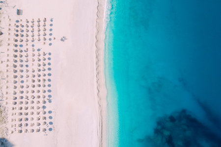 Top-down aerial view of a clean beach equipped with umbrellas and sunbeds on the turquoise sea....