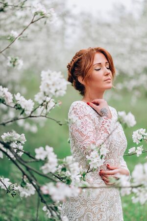 A close-up portrait of a young red-haired woman in a blossoming apple orchard.の写真素材