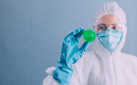 Doctor virologist in a protective suit holds a model of a coronavirus in his hands. Close up.