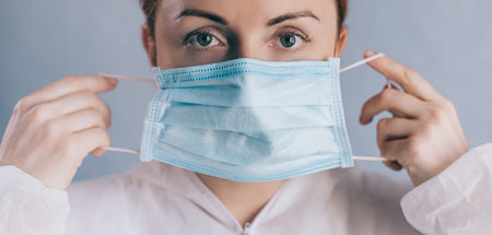 Coronavirus epidemic. A female doctor puts on a face mask and looks at the camera. Close-up.