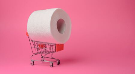 Panic purchase of toilet paper during quarantine. Roll of toilet paper in a toy trolley on a pink background. Close-up.の写真素材