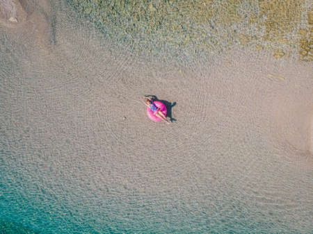 Young relaxed woman in a swimsuit swims in the water on an inflatable flamingo and sunbathes. View from above.の写真素材