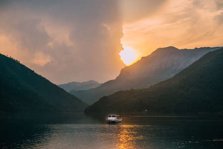 Calm landscape overlooking a mountain lake and a lone boat during sunset.の写真素材