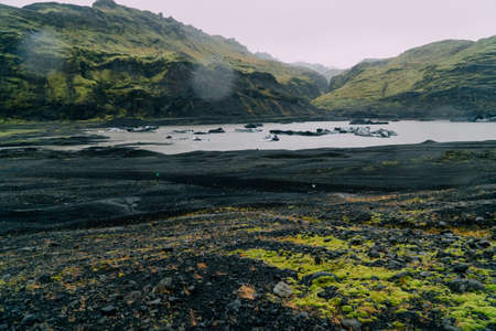 Ice floes breaking away from the melting glacier float in the lake against the backdrop of the mountains.の写真素材