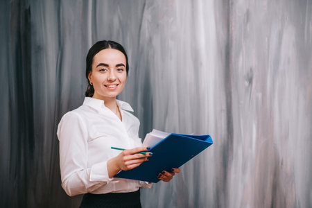 Young business female standing with folder in his hands against wall