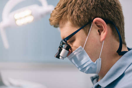 The dentist works with binocular glasses. Male doctor in a mask at work. Close-up.の写真素材