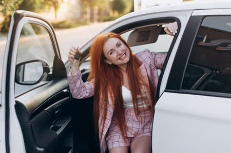 Woman bought first car. Joyful female sitting in new car and shows keys.の写真素材