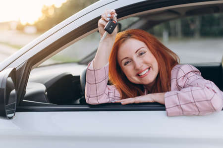Woman bought first car. Joyful female sitting in new car and shows keys.の写真素材