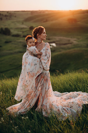 Interracial family. Young caucasian woman holding an african baby outdoors. Full-length portrait.の写真素材