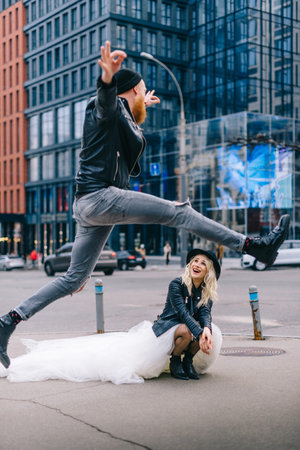 Crazy newlyweds in city. Happy groom jumping near bride on city street. Selective focus. New York,...