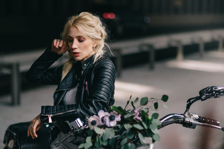 Young bride in black leather jacket sits on motorcycle, close-up portrait.