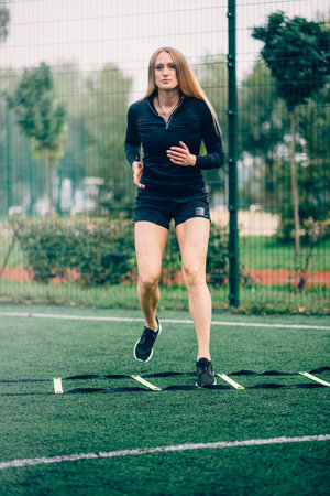 Young sportive woman trains with ladder drills .