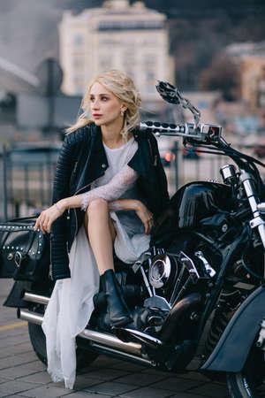 Young bride in black leather jacket sits on motorcycle, close-up portrait.の写真素材