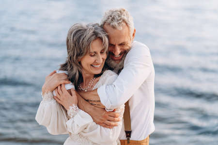 Romantic senior couple is embracing on seashore. Man hugs woman from behind.の写真素材