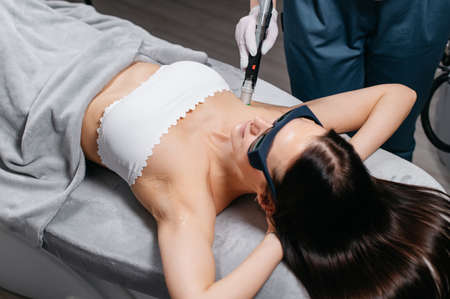 Professional cosmetologist doing armpit laser epilation to young woman in beauty salon.の写真素材