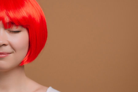 Extreme close-up of the face of a young attractive woman in a red wig with her eyes closed. Cropped shot.の写真素材