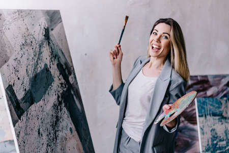Portrait of female artist. Excited woman paints a picture with a brush.の写真素材