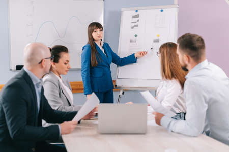 A team of business people are discussing the project together in the office. The employee shows the graphs on the board to colleagues.の写真素材