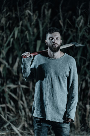 Scary man with ax stands in corn field and looks into camera at night. Halloween conceptの写真素材