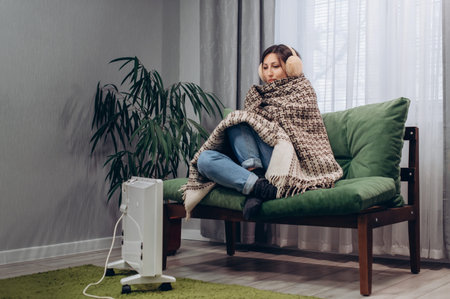 A warmly dressed young female are warming themselves near an electric radiator at home.の写真素材