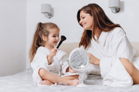 Cute preschool girl and her mom doing makeup for each other at home.の写真素材