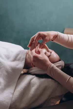 The beautician makes a deep facial massage to a young woman. Face massage technique against aging. Close-up.の写真素材