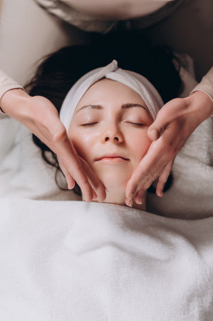 The beautician makes a deep facial massage to a young woman. Face massage technique against aging. Close-up.の写真素材