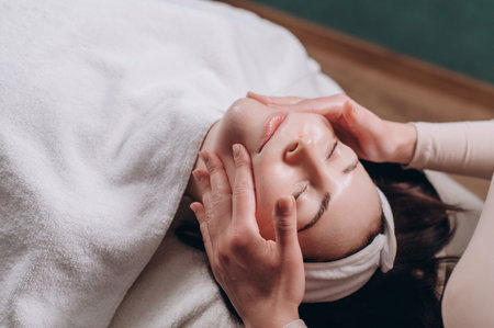 The beautician makes a deep facial massage to a young woman. Face massage technique against aging. Close-up.の写真素材