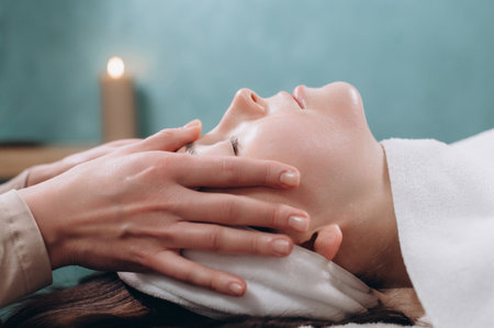The beautician makes a deep facial massage to a young woman. Face massage technique against aging. Close-up.の写真素材