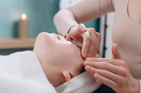 The beautician makes a deep facial massage to a young woman. Face massage technique against aging. Close-up.の写真素材