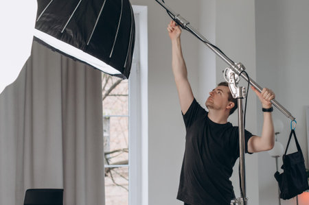 A professional photographer adjusts studio lighting equipment with a boom arm and softbox, preparing a modern indoor photoshoot setup.の写真素材