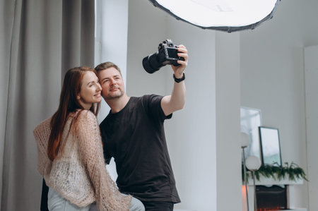 A photographer and a female model take a selfie together in a professional studio, smiling during a relaxed behind-the-scenes photoshoot moment.の写真素材