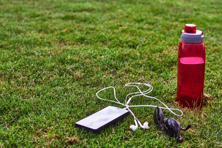 phone headphone water bottle and sunglasses on the grassの写真素材