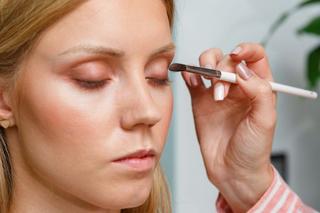 The process of creating makeup. Makeup artist working with a brush on the face of the model.
