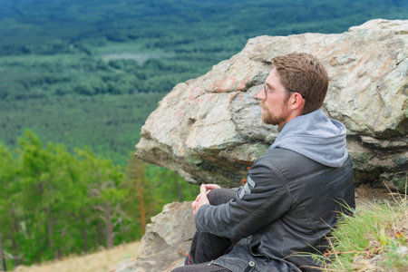 The guy sits on the top of the mountain and enjoys the beautiful view of nature.